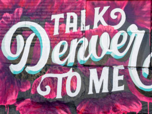 A street mural in Denver, Colorado, featuring pink flowers behind the saying "Talk Denver to Me"