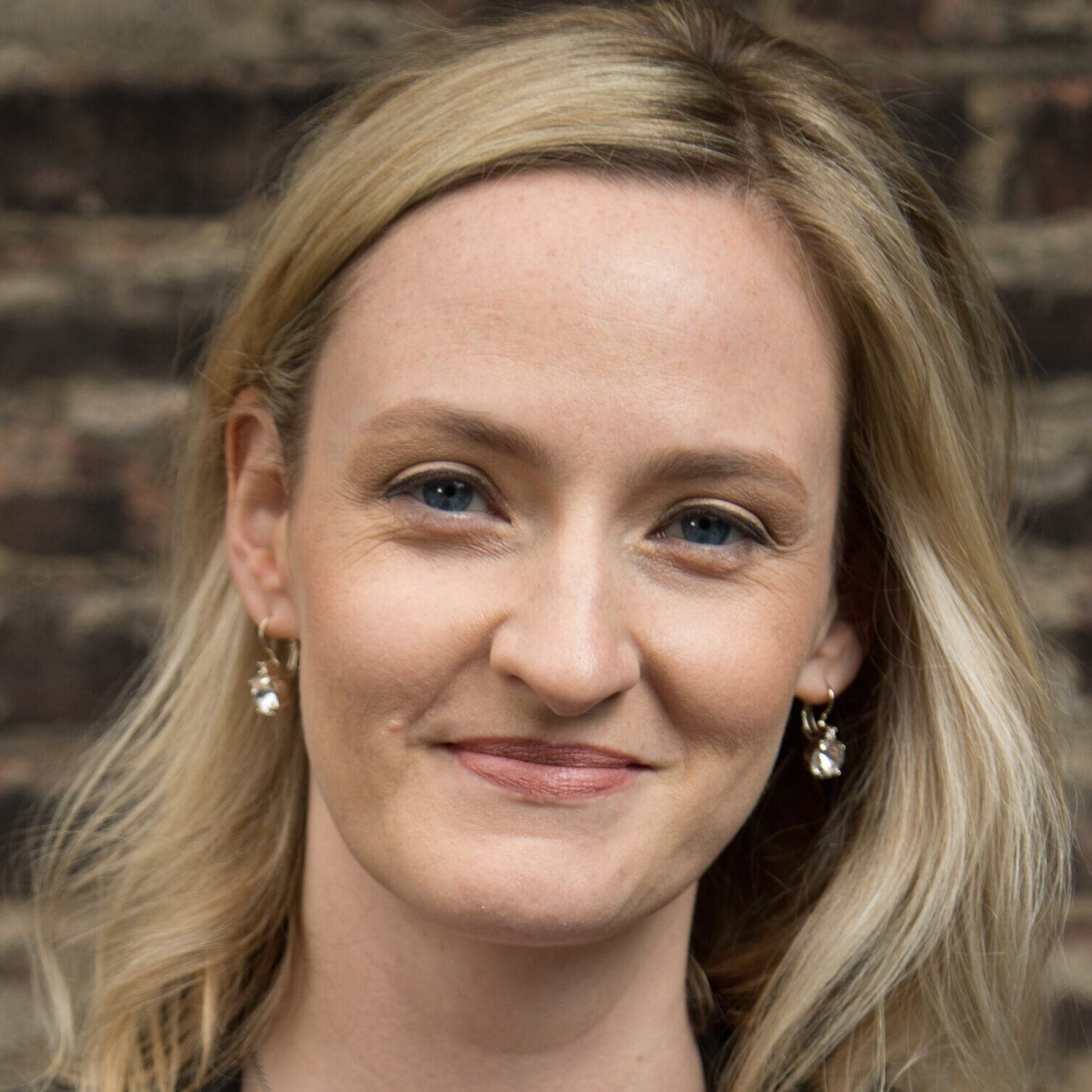 Asha Curran has medium blonde hair and is wearing gold earrings in her headshot photo