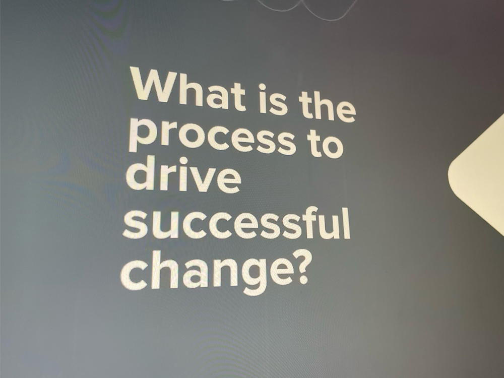 A shot of the presentation, which is cream text on a dark gray background. It reads, "What is the process to drive successful change?"