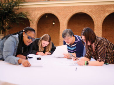 Four people huddle around a table in front of a brick building during a Bainum Family Foundation retreat.