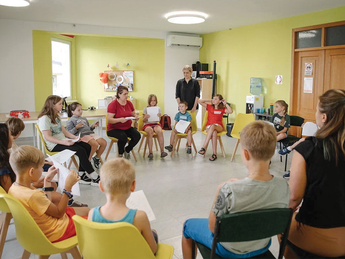 A group of children and teachers sit around a circle in a pale yellow room in Chisinau, Moldova.