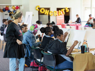 Teenagers paint on blank canvasses while an instructor looks on. A gold balloon sign reads "Congrats" in the background.
