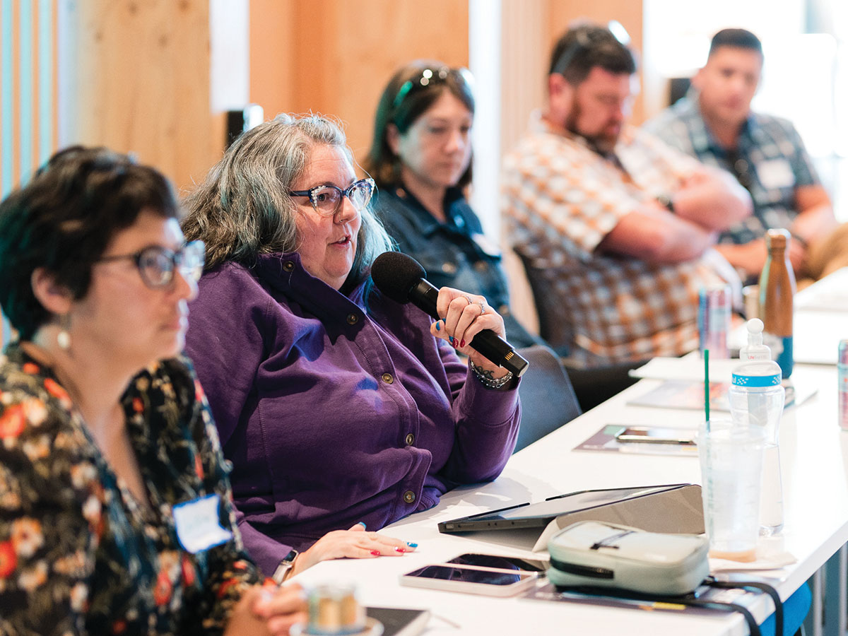 A woman in a purple shirt speaks into a microphone.