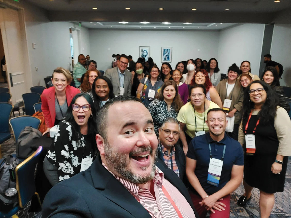 Rafael Torres takes a selfie picture of himself standing in front of PEAK's Latinx Caucus.