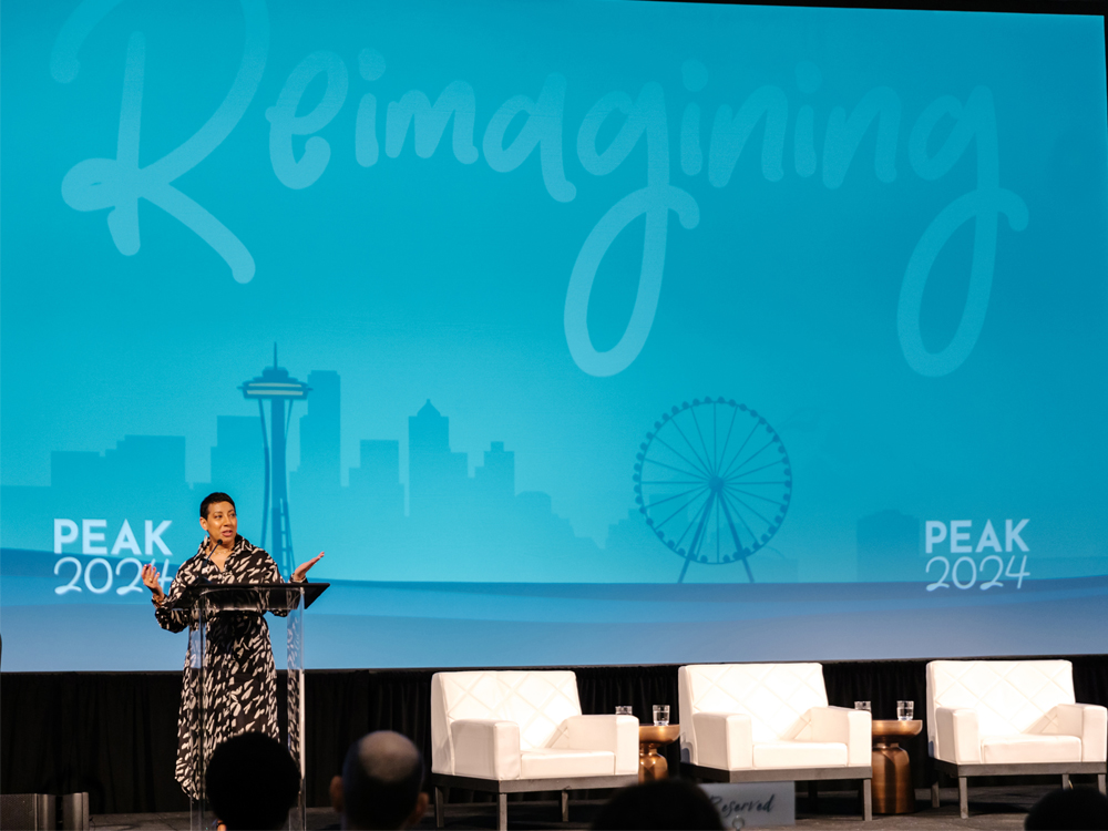 A photograph of PEAK CEO and President Satonya Fair speaking from a podium on stage at PEAK2024