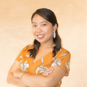 Jennelyn Tumalad is standing in front of a yellow background, wearing a yellow and white patterned blouse.