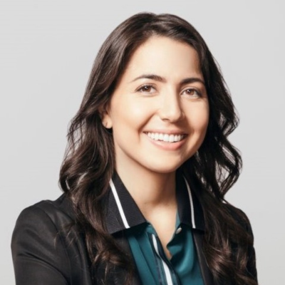 June Palacios is a young Latina woman with a wavy shoulder length bob hairstyle. She is smiling openly in this photo and wears a hunter green blouse with a black collar with a white stripe and a black blazer.