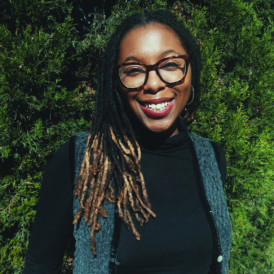 La Keisha smiles in her headshot in front of green foliage.