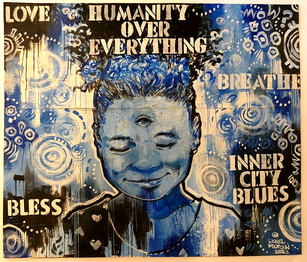 This painting shows a young Black girl painted in blues, blacks, and creams. Her eyes are closed, but a third eye is opened on her forehead. The phrases "Humanity over everything," "Breathe," "Inner City Blues," and "Bless" are stenciled in.