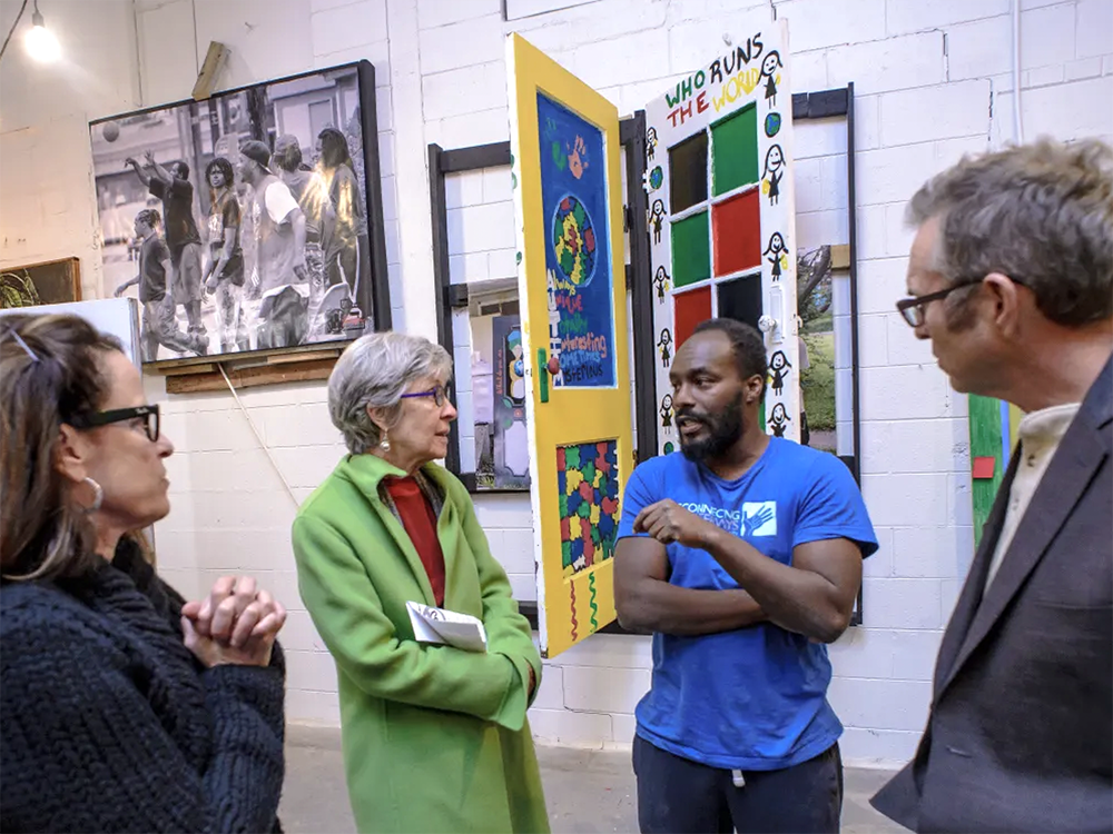A photo of De'Amon Harges talking to a group of three people at the art gallery show Perception: What's Behind the Door
