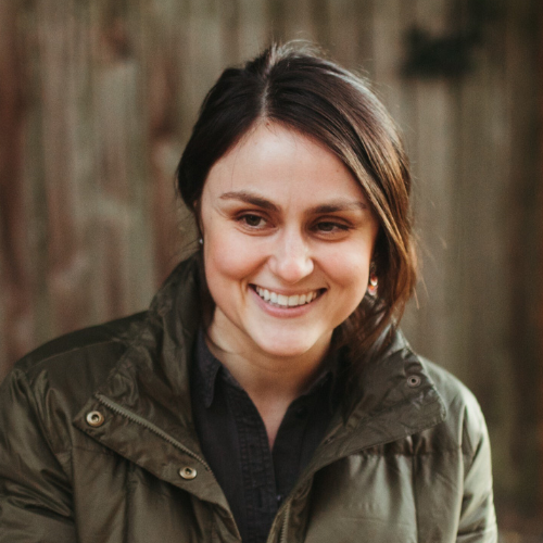 Vanessa Elkan is smiling with in this photo, her hair is swept back. She is wearing a black scarf under an army green jacket.