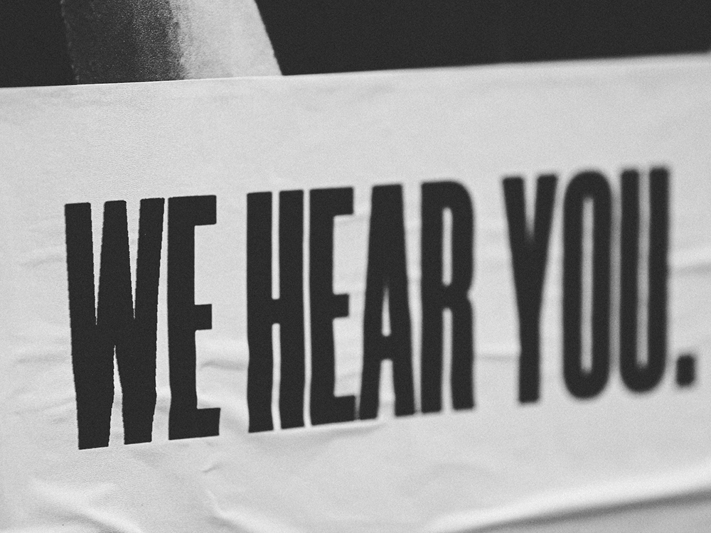 A black and white photo of a sign with the words "We Hear You"