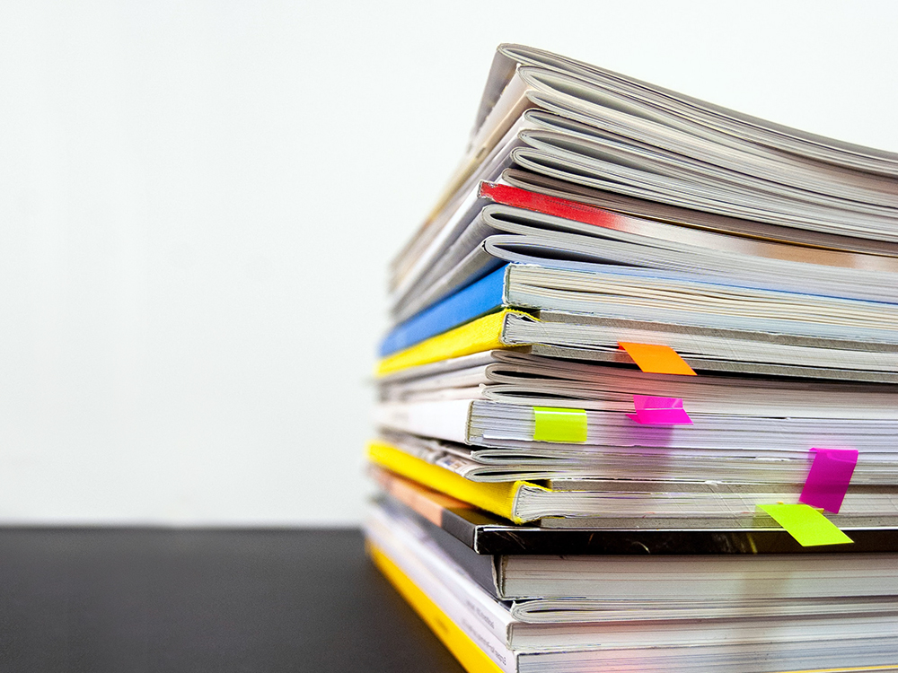 This image shows a stack of soft cover reports. Various notes poke out of the pages.