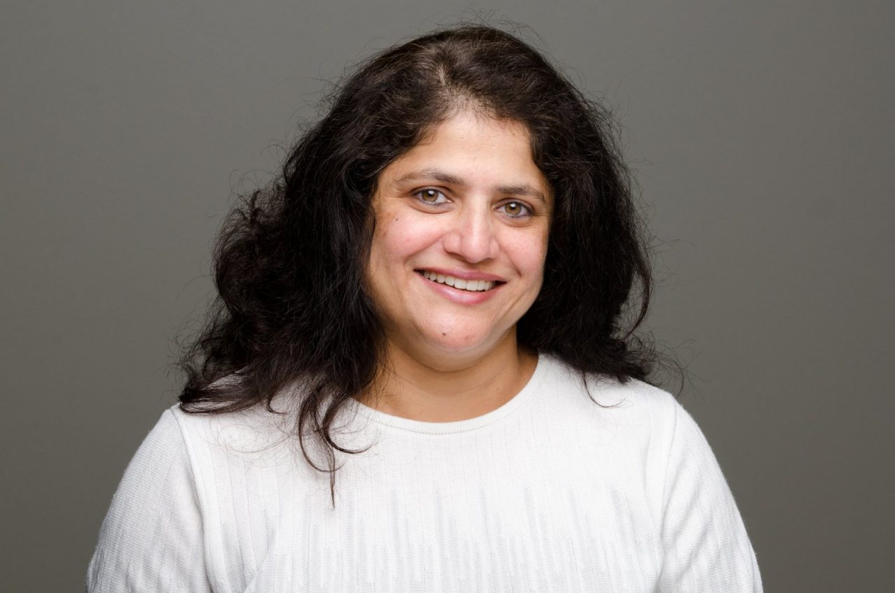 Roshani Desai wears a white shirt and smiles at the camera in her headshot picture