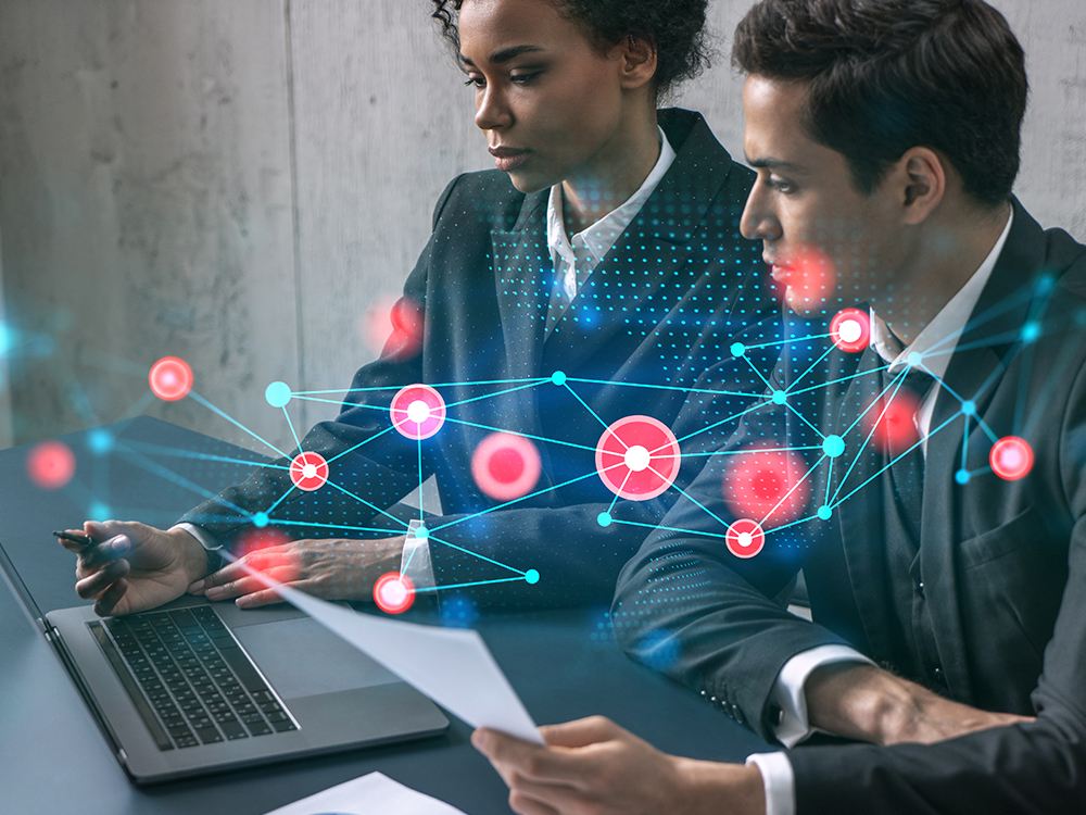 An illustration of a web of plot points superimposed on a photo of two colleagues working at a computer