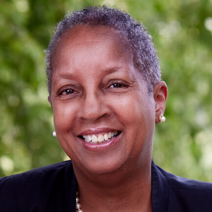 Monica Thorns smiles in her headshot picture in front of green foliage